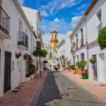 Flower-lined alley in Estepona old town with a church tower in the background