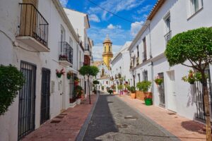 Flower-lined alley in Estepona old town with a church tower in the background