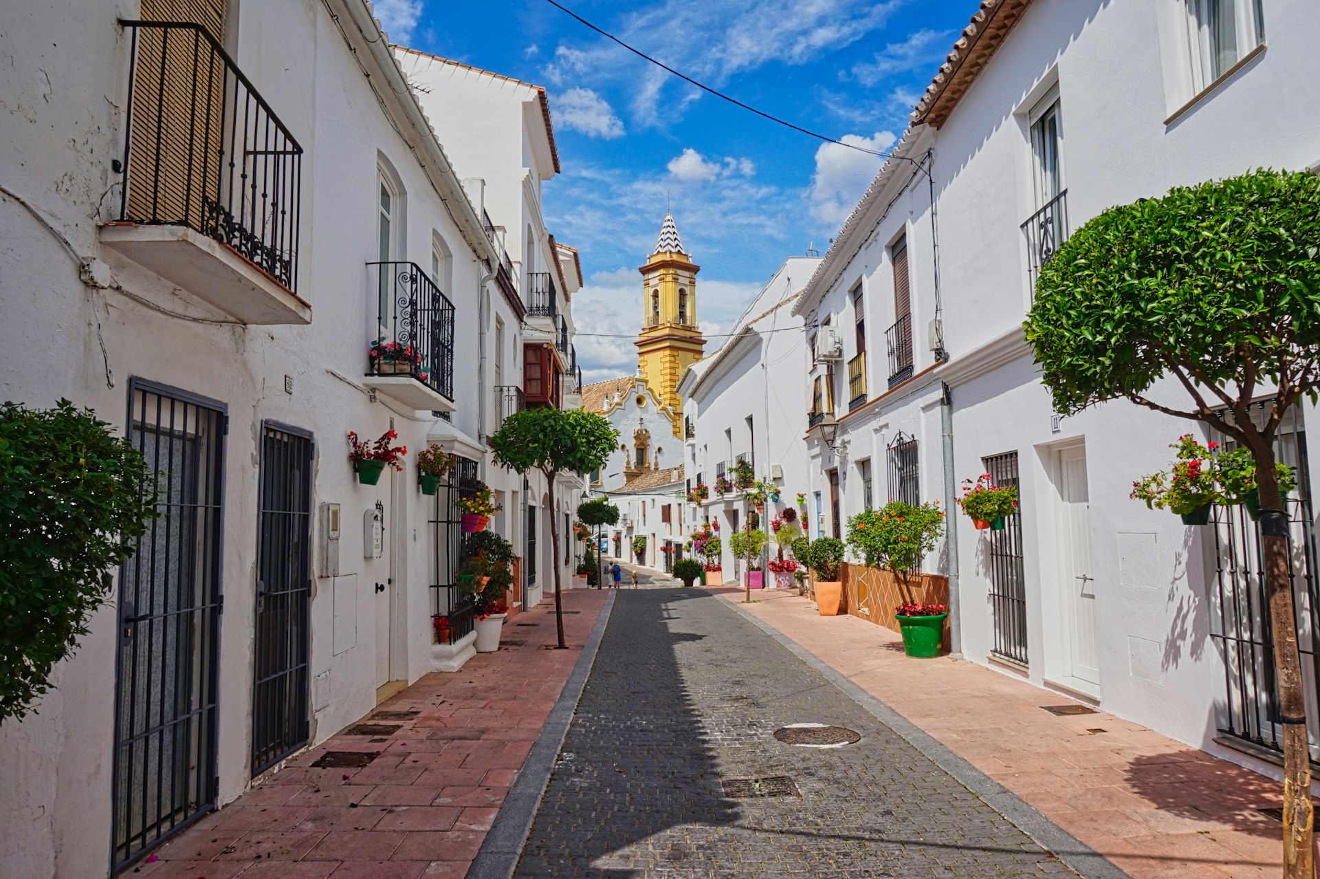 Flower-lined alley in Estepona old town with a church tower in the background