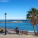 Couple walking along a sunny seafront promenade on the Costa del Sol, Spain