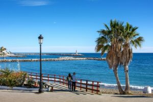Couple walking along a sunny seafront promenade on the Costa del Sol, Spain