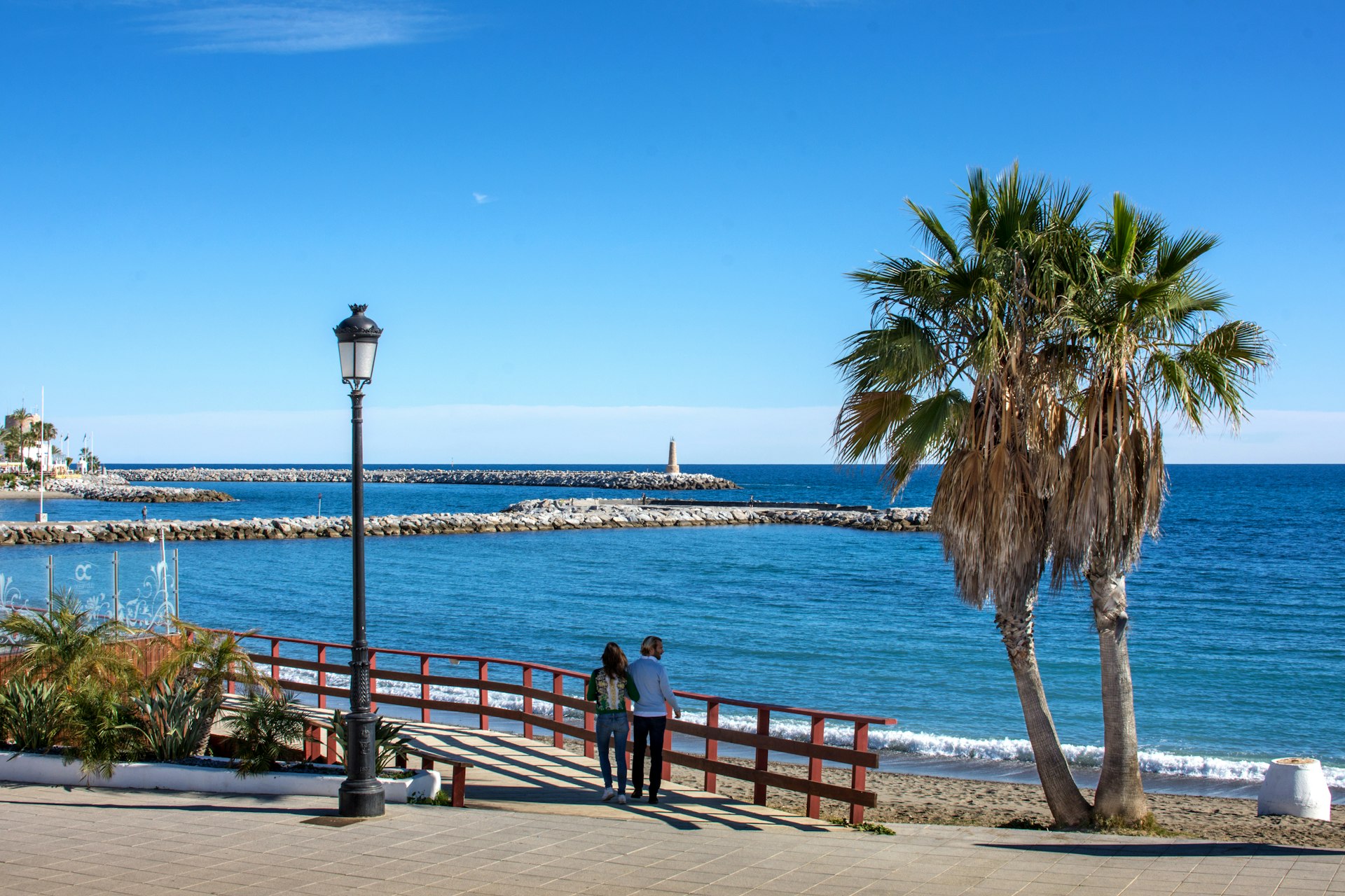 Couple walking along a sunny seafront promenade on the Costa del Sol, Spain