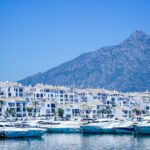 Blue and white boats on the Mediterranean coast of Spain near mountains and a clear blue sky