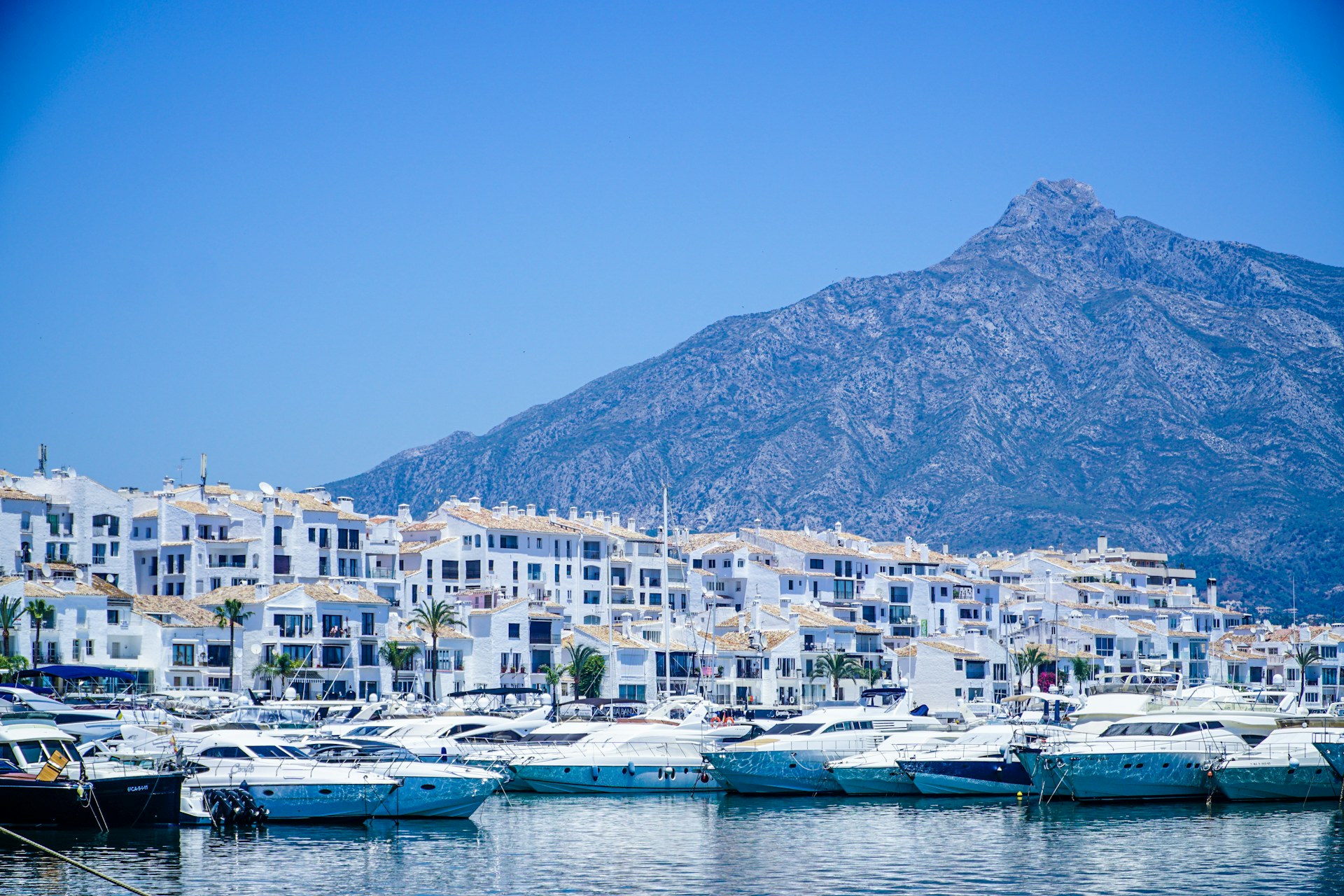 Blue and white boats on the Mediterranean coast of Spain near mountains and a clear blue sky